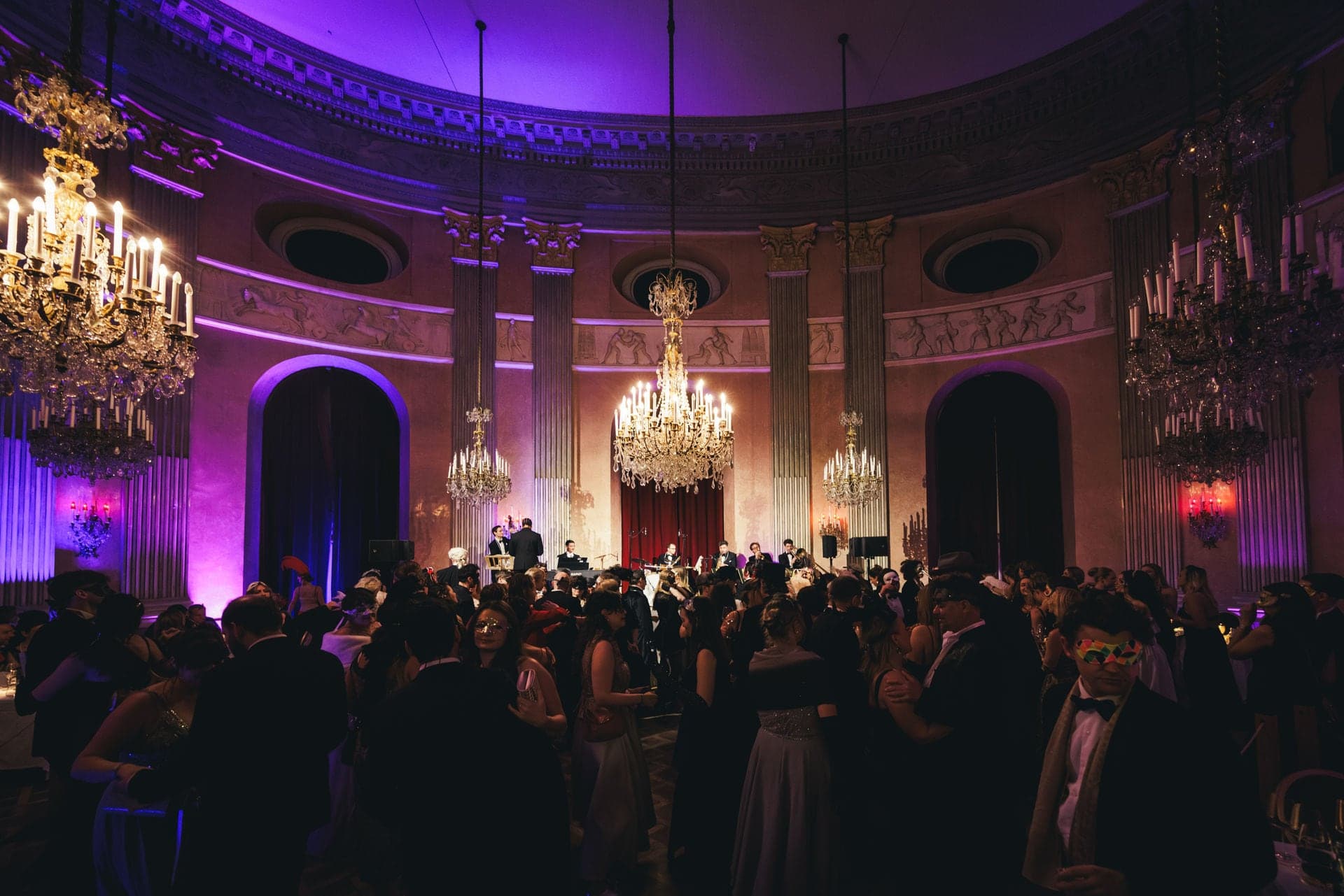 Volle Tanzfläche im Hauptsaal des Palais unter violettem Licht und Kristallustern