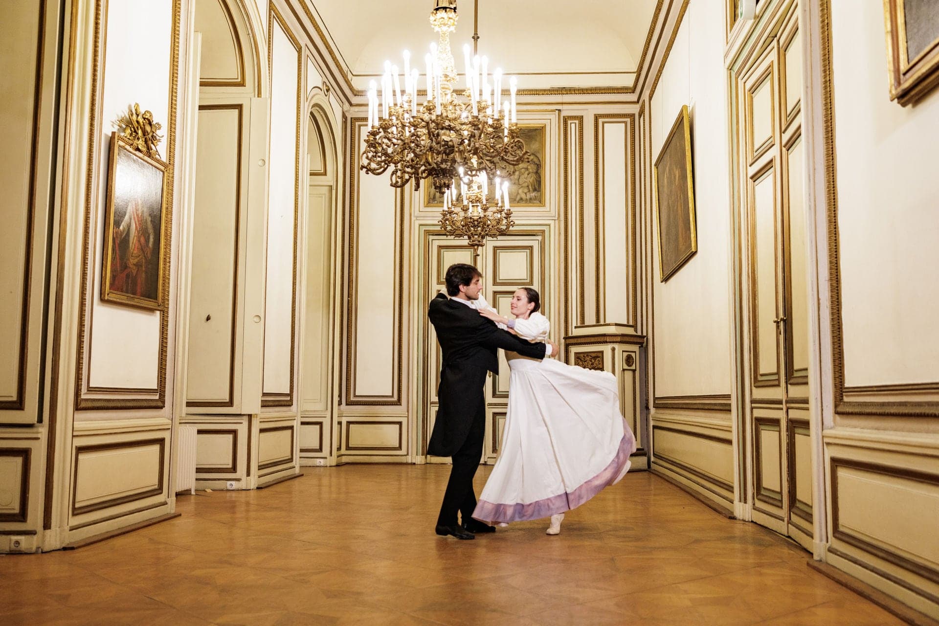 Walzerpaar im Frack und weißen Ballkleid in einem Salon mit Kristalllüster