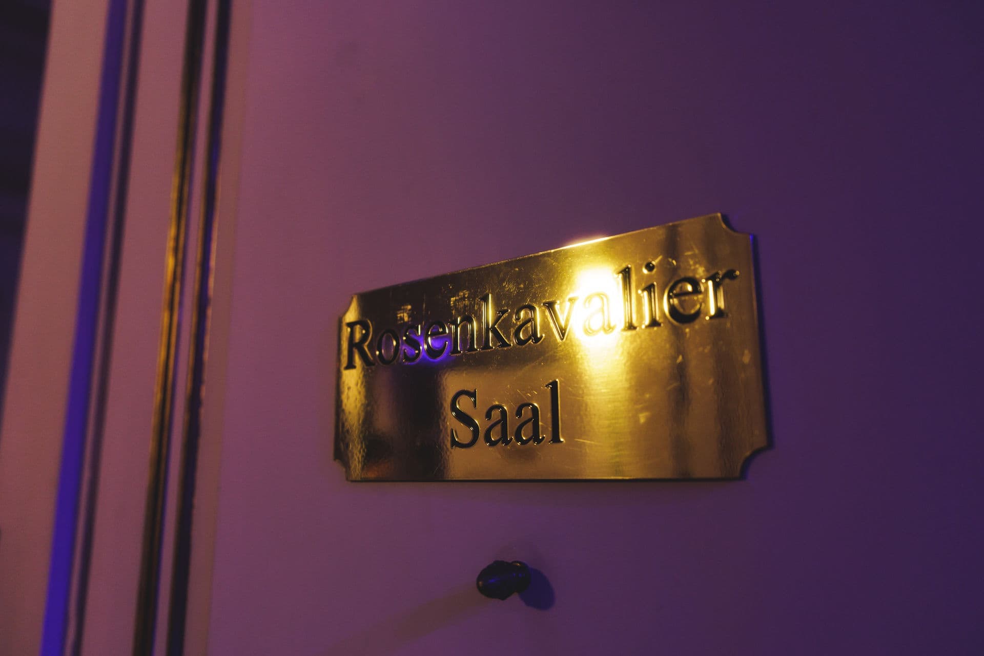 Messingschild „Rosenkavalier Saal“ an einer Tür in violettem Licht
