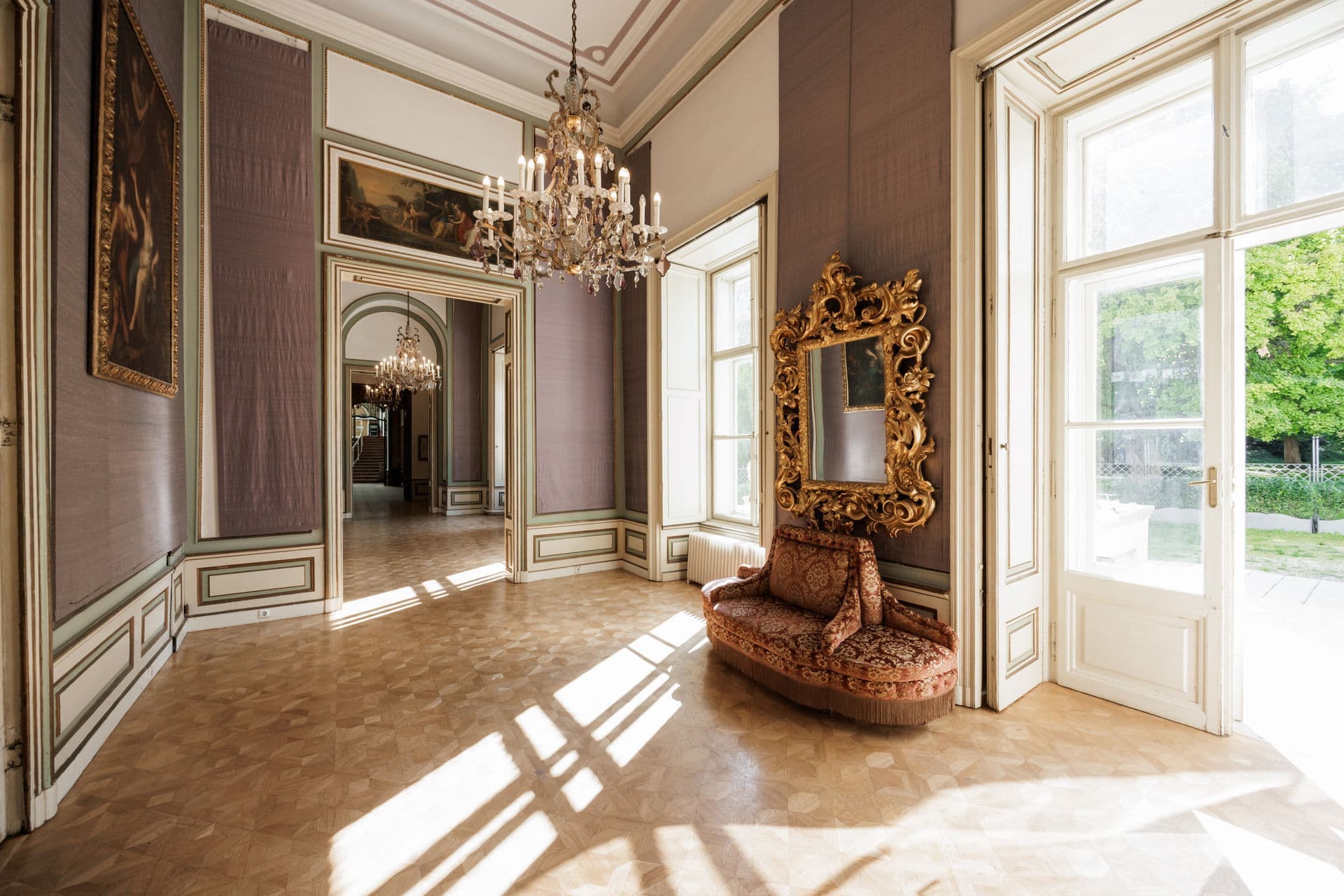 Heller Salon mit Kristallluster, goldgerahmtem Spiegel und hohen Fenstern